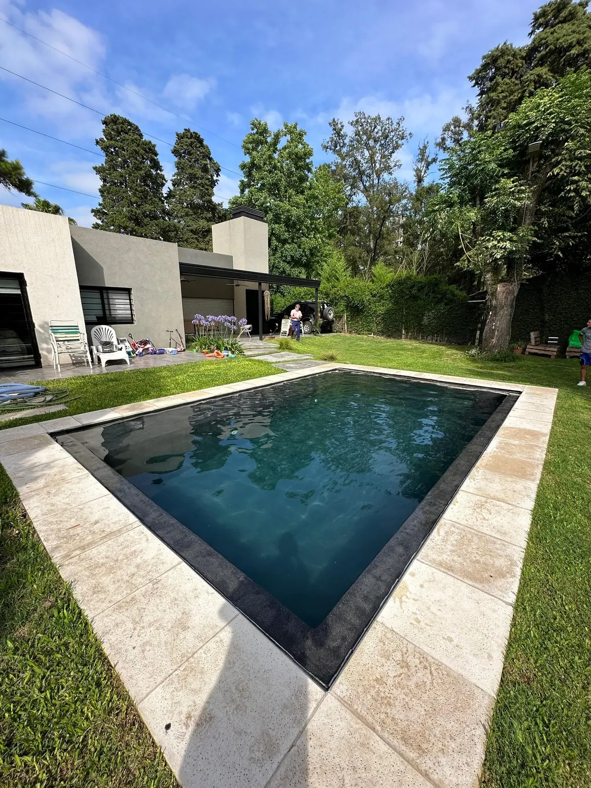 Piscina de borde finlandés con terminación oscura y solado de piedra clara frente a una casa