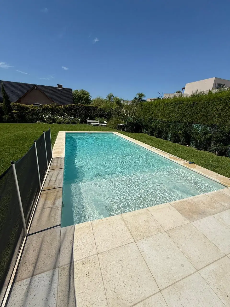 Piscina larga de agua turquesa con solado de piedra clara en un jardín