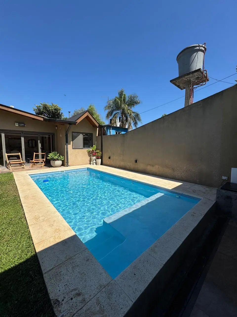 Piscina rectangular de agua celeste con escalones y banco bajo el agua, junto a una medianera alta