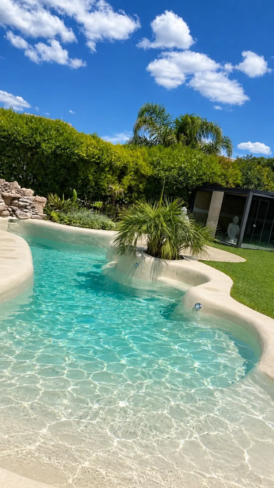 Piscina de arena de Diego Di Lullo terminada, con agua turquesa, isla de palmeras y cascada de piedras