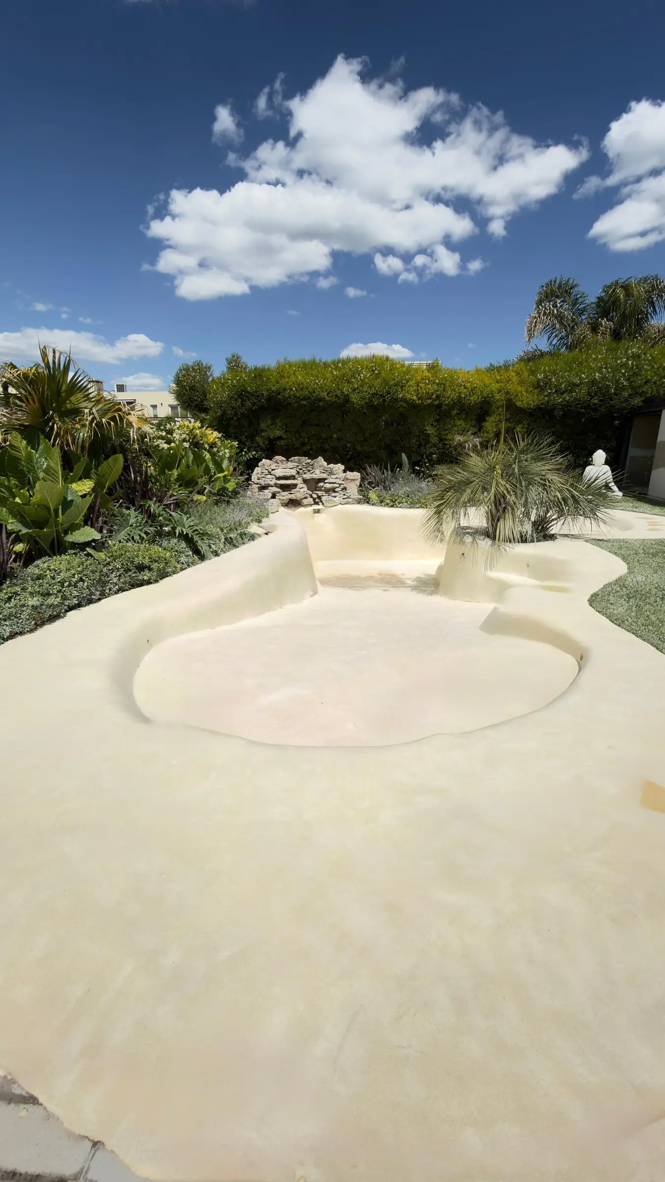 Piscina de arena de formas libres rodeada de jardín, antes del llenado