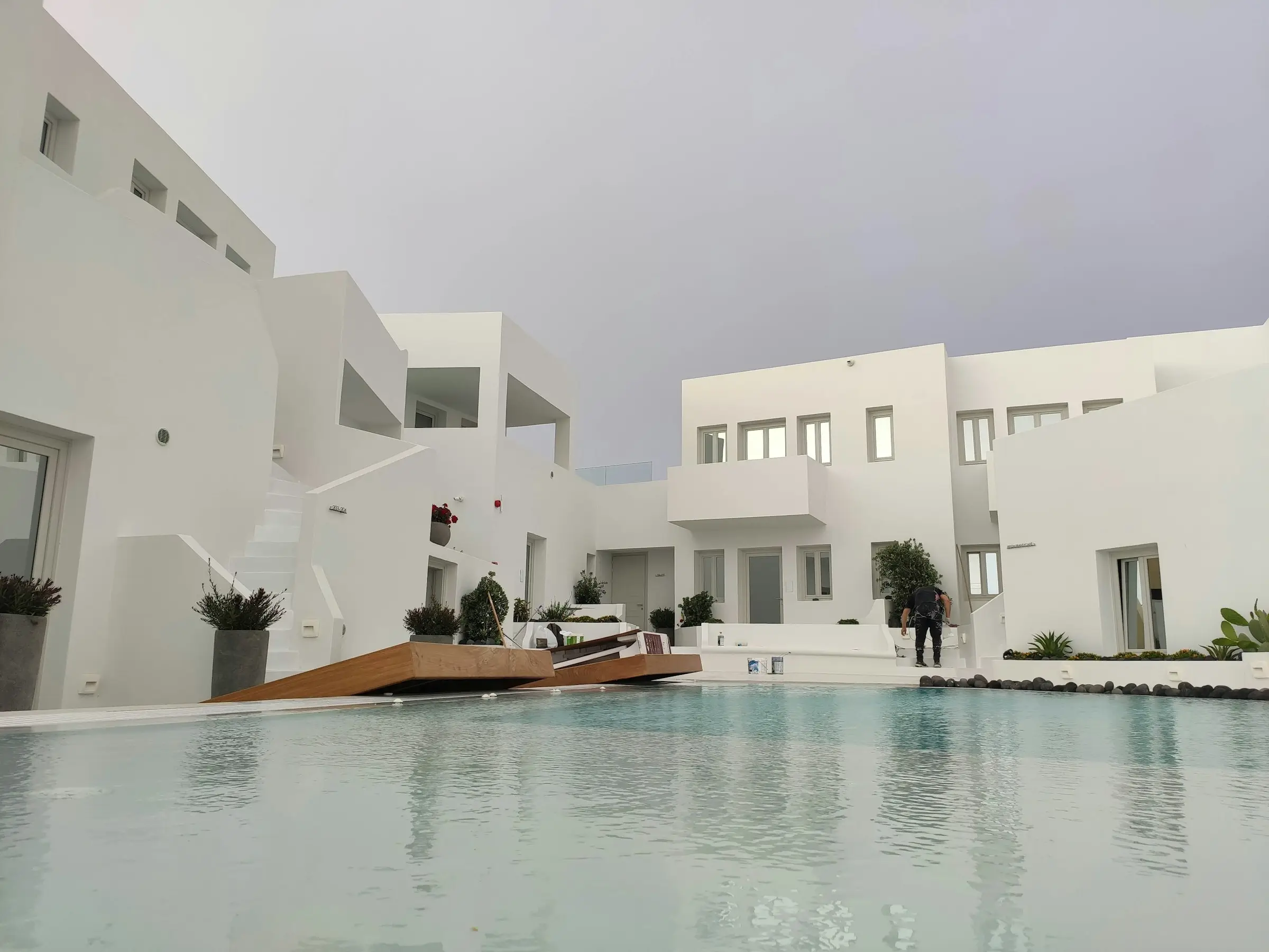 Piscina con el agua al ras del solado reflejando casas blancas