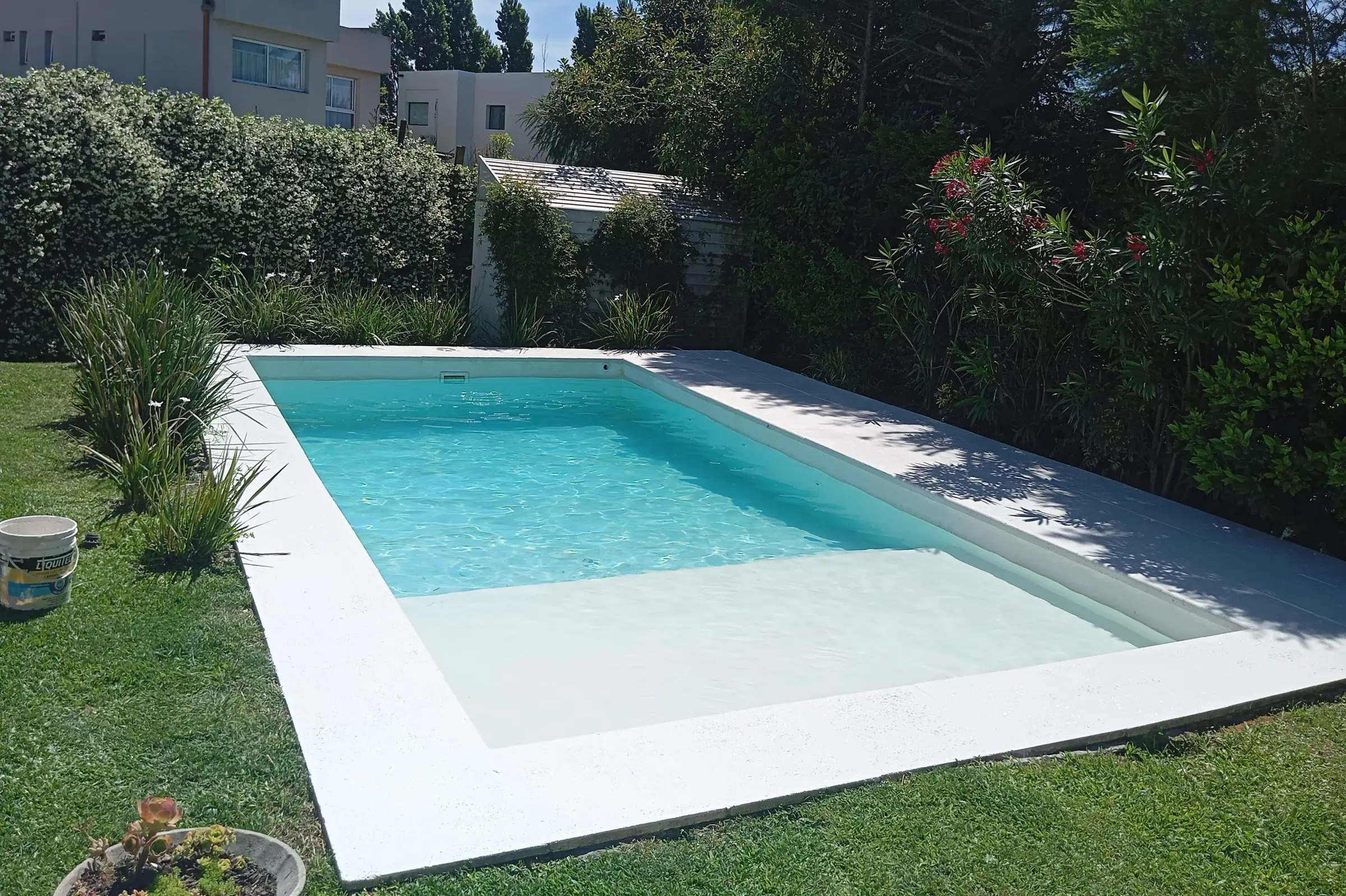 Piscina con un sector de poca profundidad de fondo blanco y borde claro en un jardín