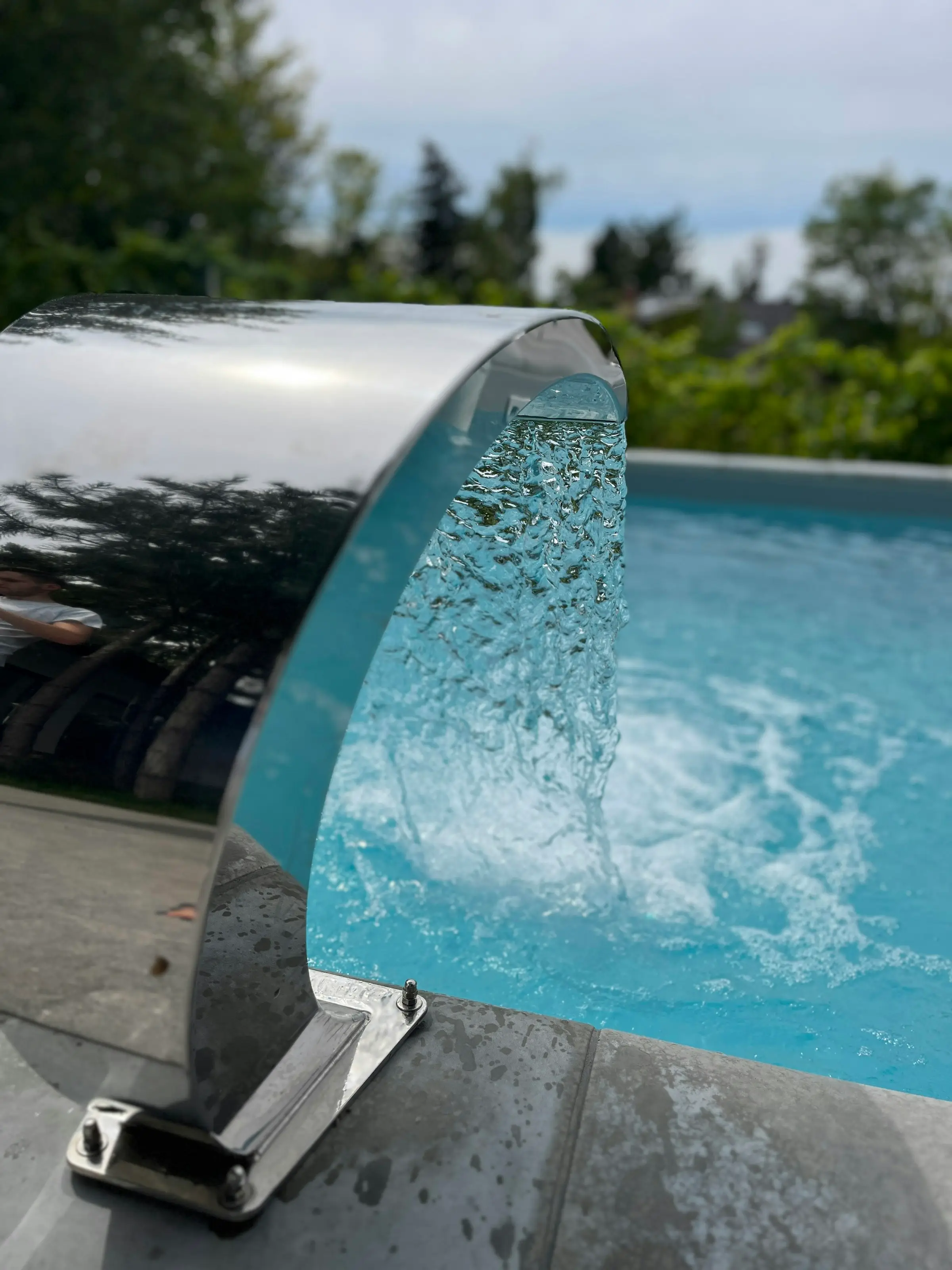 Cascada de acero inoxidable que vuelca agua sobre una piscina