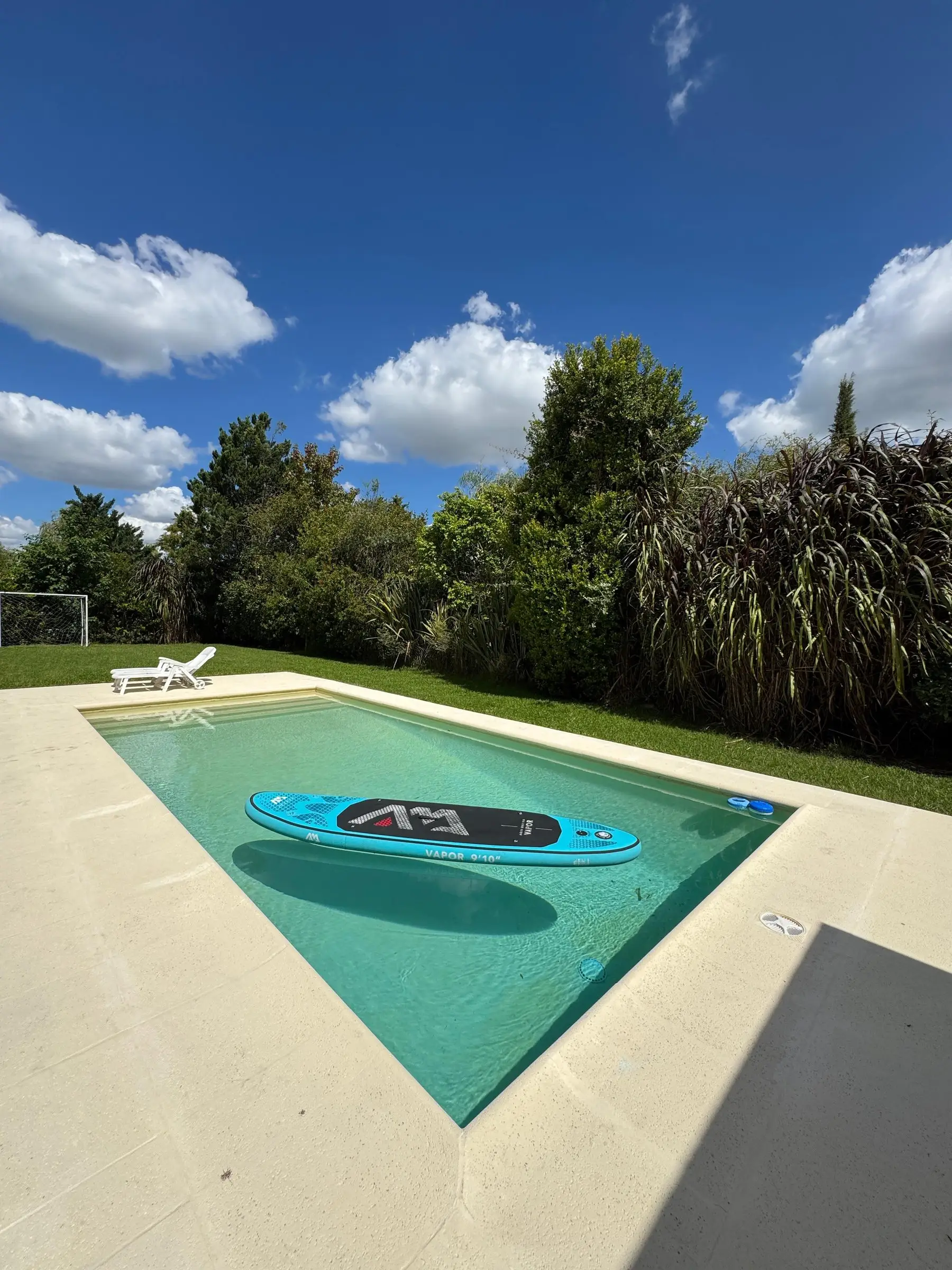 Solárium amplio color arena alrededor de una piscina de agua verde clara